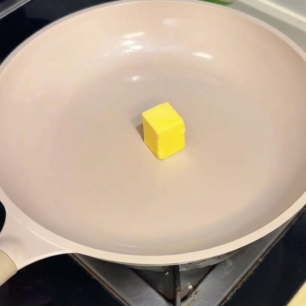 A single square of yellow butter sliding across the surface of a warm, cream-colored non-stick pan.