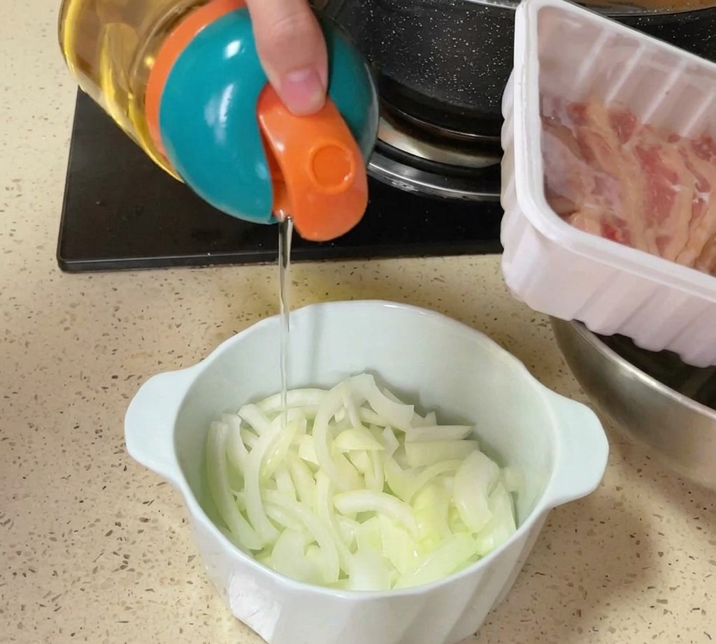 A colorful handheld dispenser pouring oil or salt over a bowl of sliced raw onions on a kitchen counter.