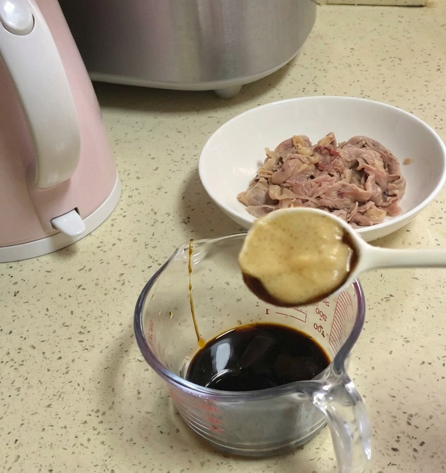 A white spoon holding a dollop of honey over a glass measuring cup filled with a dark soy sauce mixture.