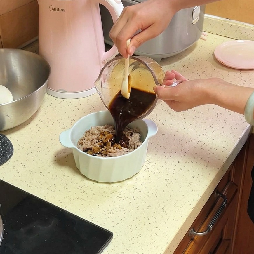 A dark brown savory sauce being poured from a glass measuring cup onto thin slices of beef and onions in a white ceramic bowl.