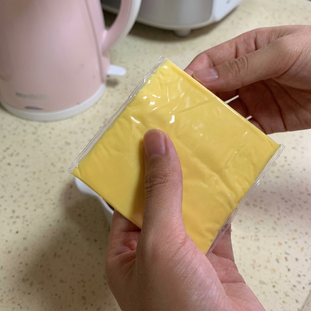A person holding two square slices of bright yellow processed cheese over a bowl filled with beef and dark sauce.