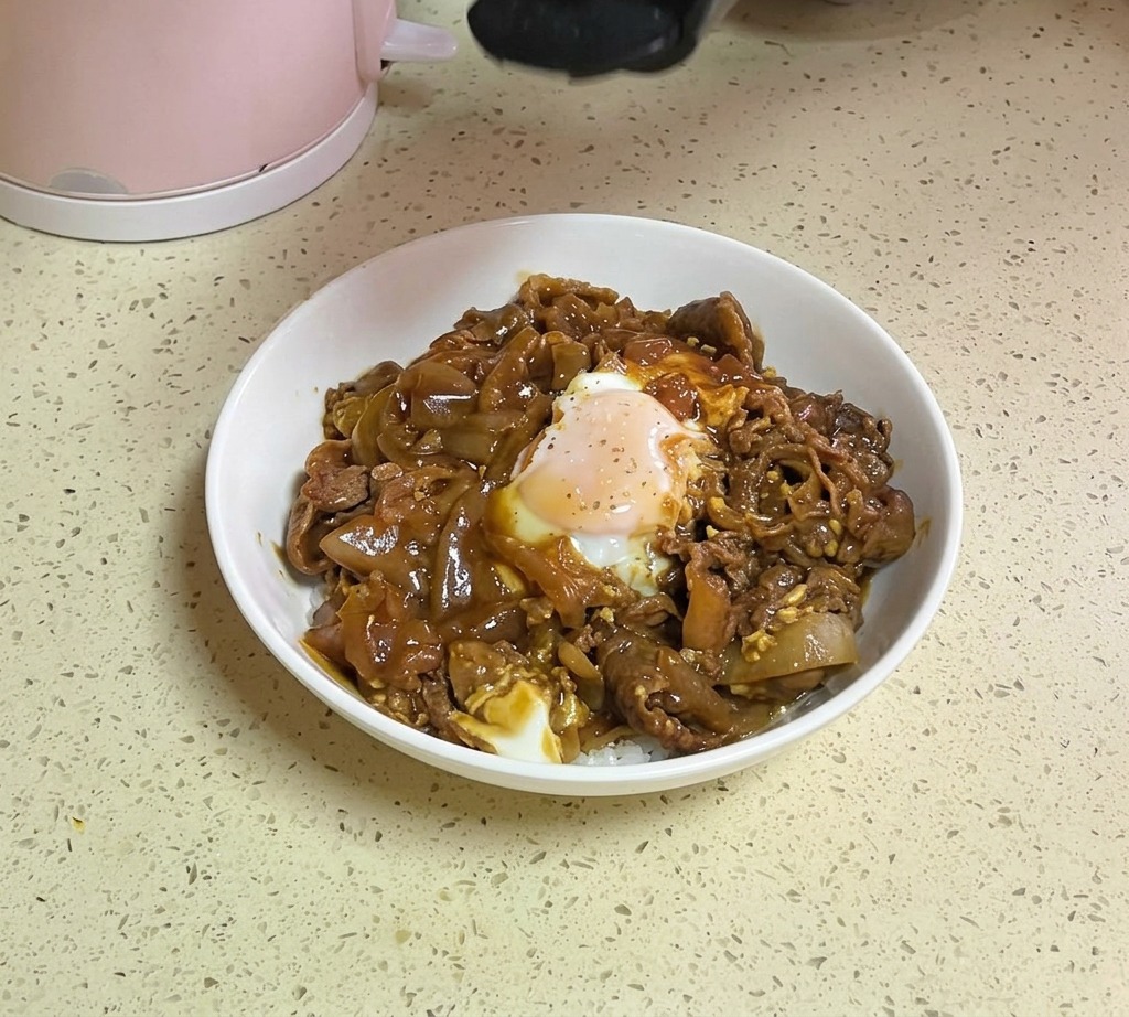 A hand shaking white sesame seeds and green parsley flakes from a container onto a finished beef and egg rice bowl.