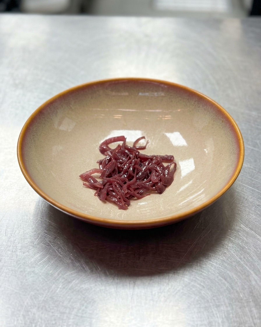 A small mound of shredded purple onions placed in the center of an empty wide beige ceramic bowl.