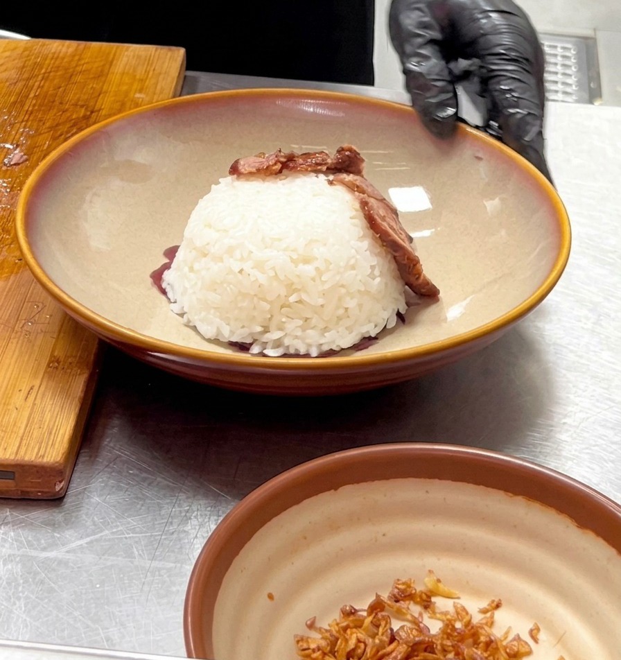 A gloved hand placing a slice of cooked beef onto a dome of white rice to build a volcano shape.