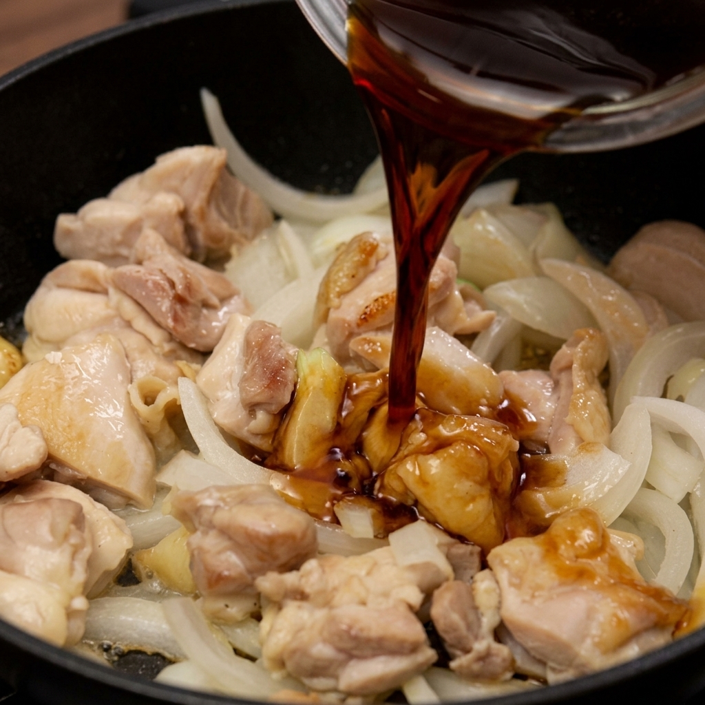 A dark soy-based sauce being poured into a pan with sautéed chicken and sliced white onions.