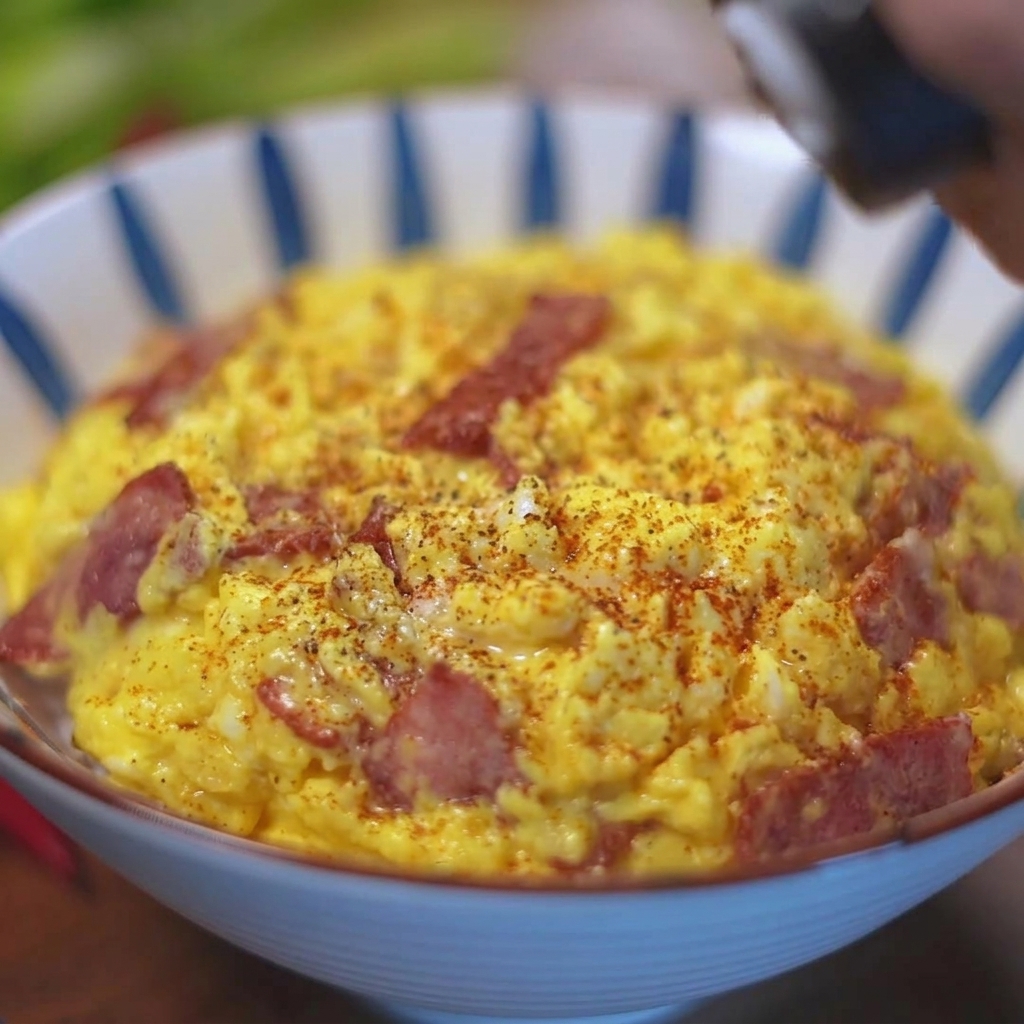 Fresh black pepper being ground onto a bowl of scrambled eggs and bacon on a bed of rice.