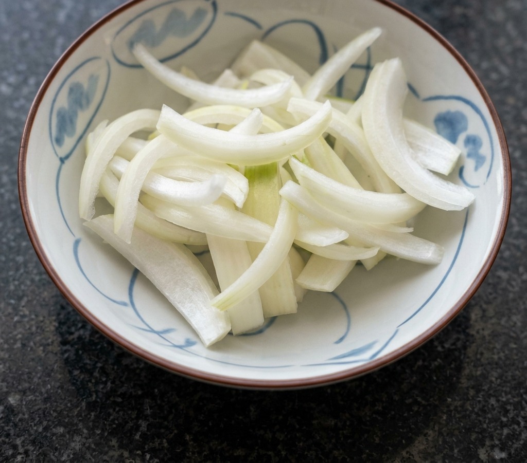 A white ceramic bowl with blue patterns filled with a pile of freshly sliced white onion crescents.