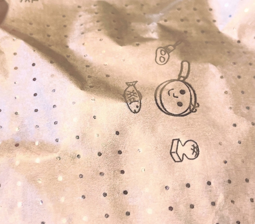 A close-up view of a circular cooking paper lid with illustrated kitchen motifs covering a pan during the steaming process.