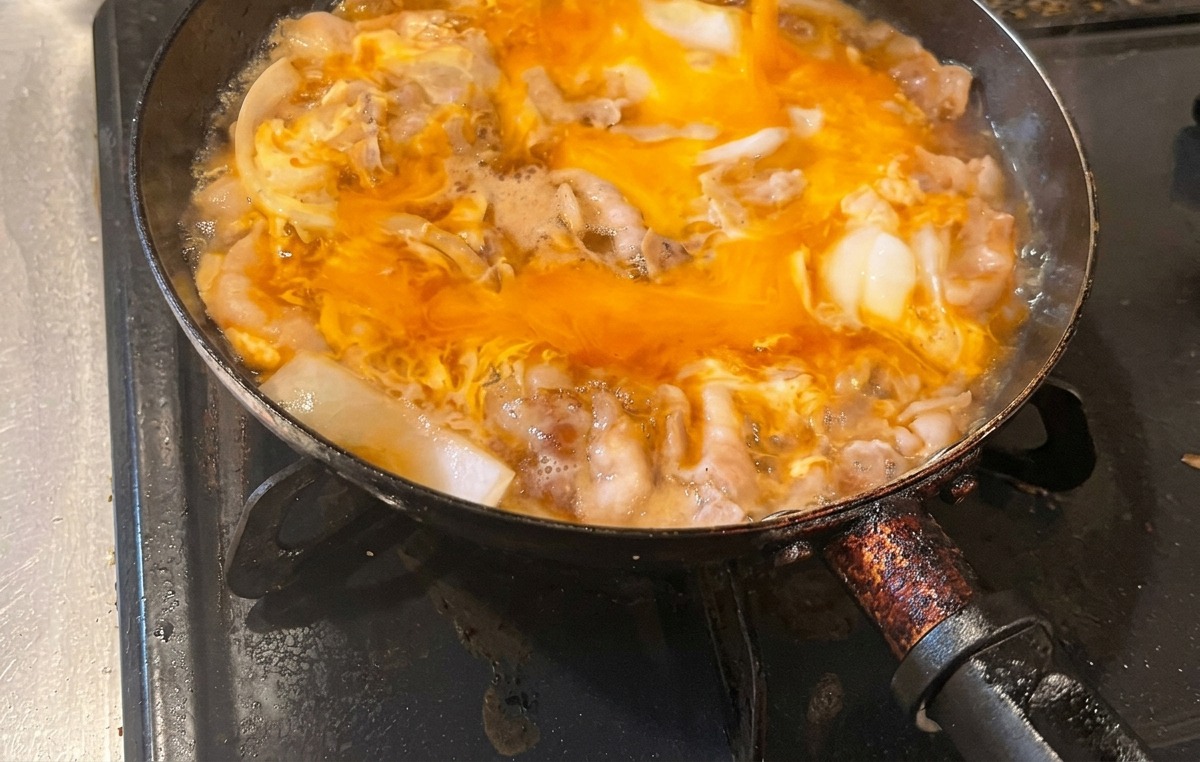 The second half of the beaten egg mixture being poured into the pan over the already partially cooked egg and meat base.