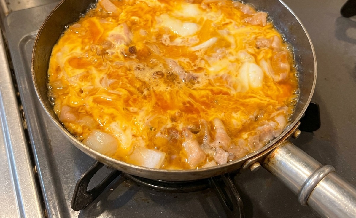 A pan of Tanindon simmering on the stove, with the yellow eggs becoming opaque and perfectly set around the pork and onions.