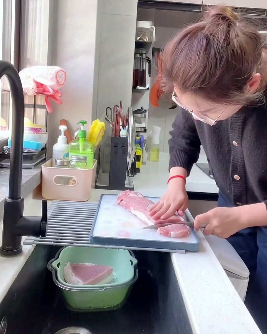 A person using a kitchen knife to cut a long strip of raw pork loin into thick, 1cm slices on a white cutting board.