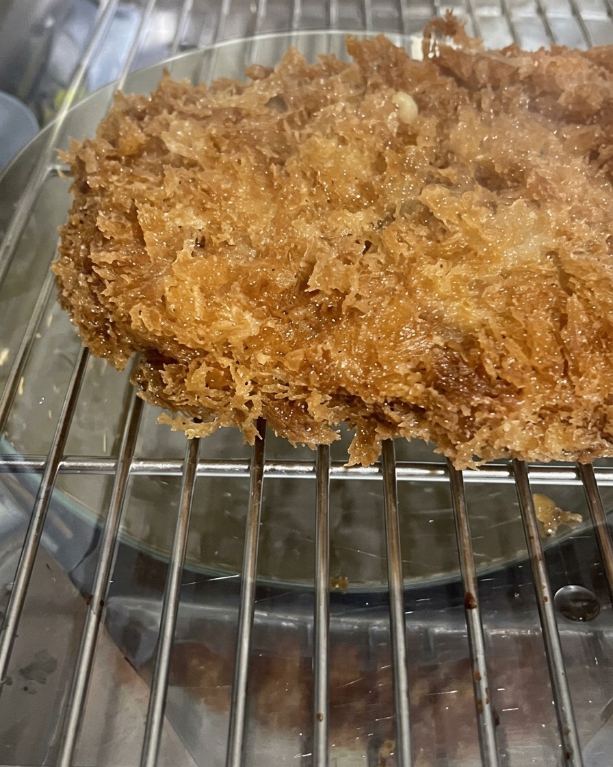 A close-up view of a fried pork cutlet covered in crispy, jagged panko breadcrumbs resting on a metal wire rack.