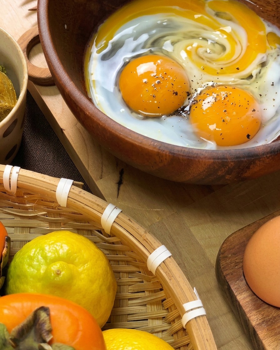 Fresh eggs cracked into a wooden bowl with visible black pepper and a splash of milk, ready to be whisked.