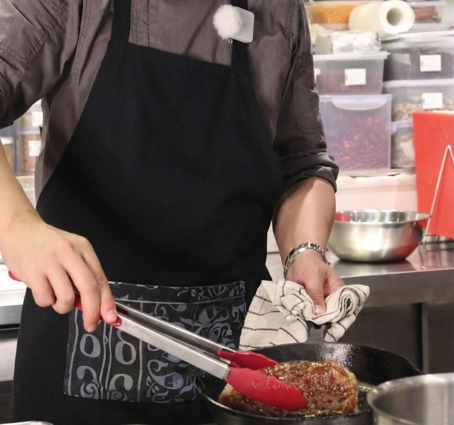 Close-up of a large beef block being held vertically with red-tipped tongs in a hot cast-iron skillet.