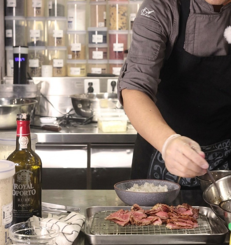 A gloved hand drizzling dark yakiniku sauce from a spoon over a bowl of steamed white rice.