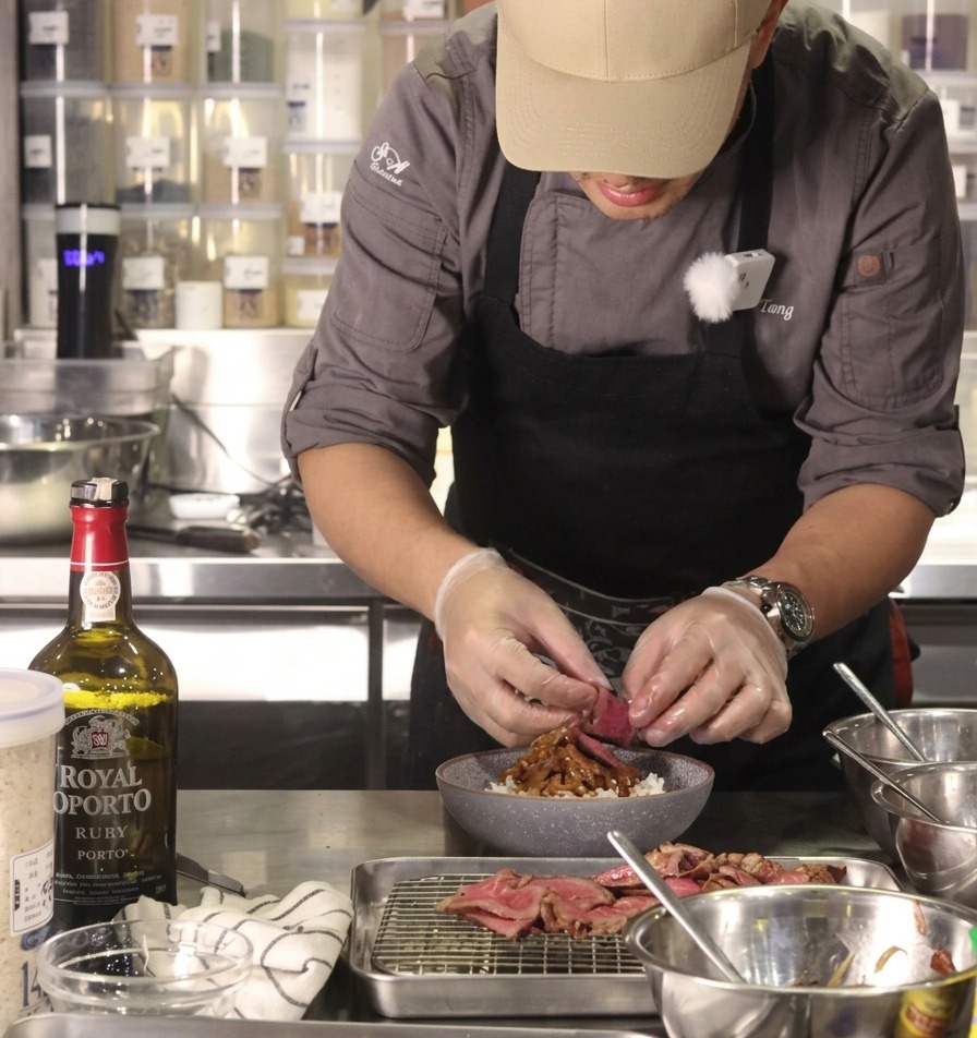 The chef placing a slice of medium-rare beef at the base of a rice bowl filled with caramelized onions.