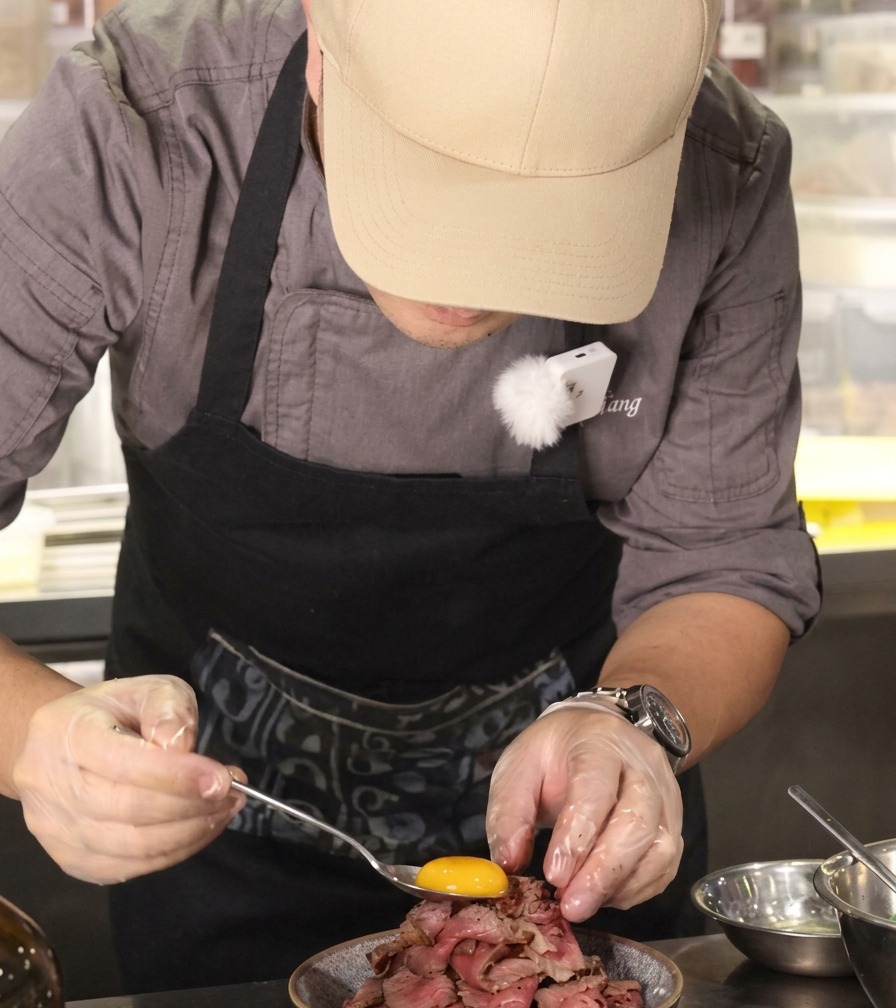 A bright orange raw egg yolk being placed onto the peak of a stacked beef mountain bowl.