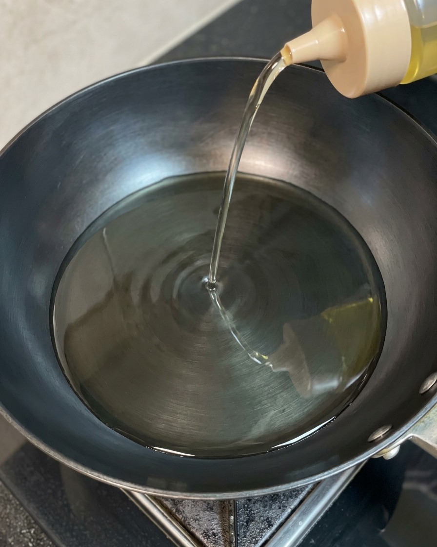 Clear cooking oil being poured from a squeeze bottle into a dark, heated wok.