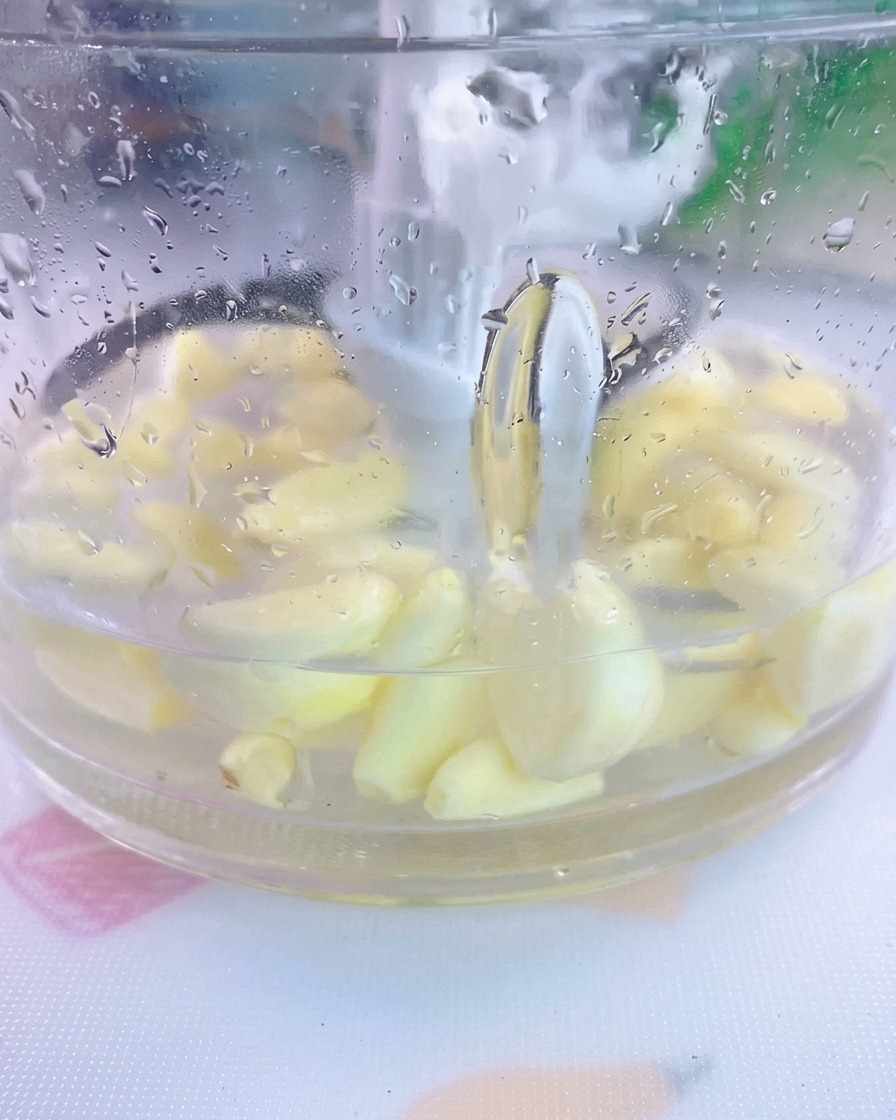 Peeled garlic cloves and salt submerged in water inside a transparent blender jar.