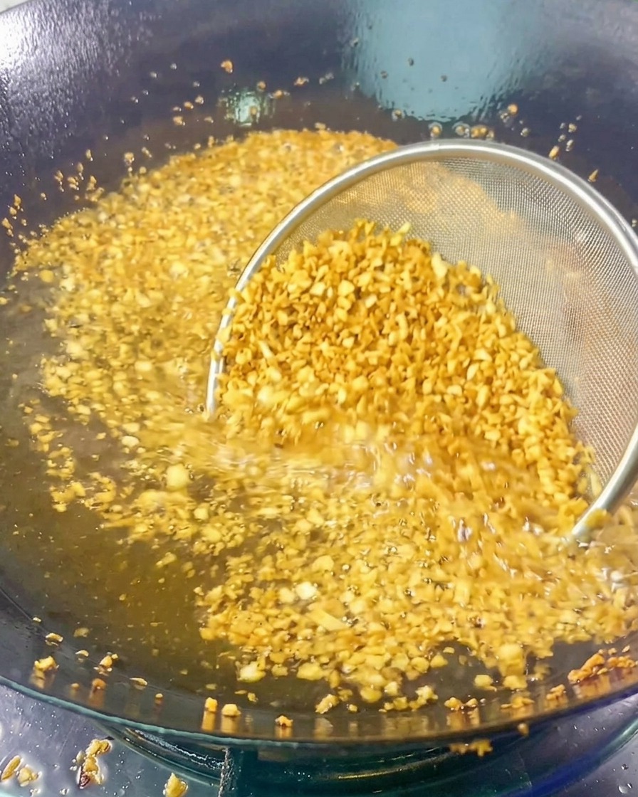 A mesh strainer filled with minced garlic submerged in hot frying oil as it turns golden and fragrant.