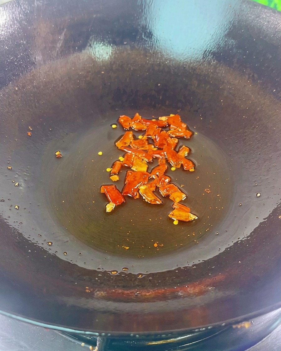 Dried red chili pieces and black beans sizzling in the bottom of a dark wok with a light coating of oil.