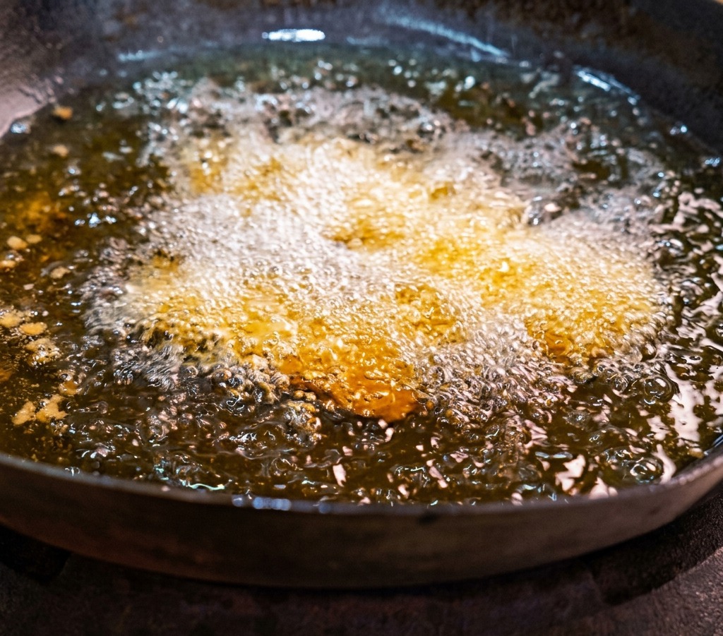 Slices of marinated pork belly being deep-fried in a wok of hot, bubbling oil.