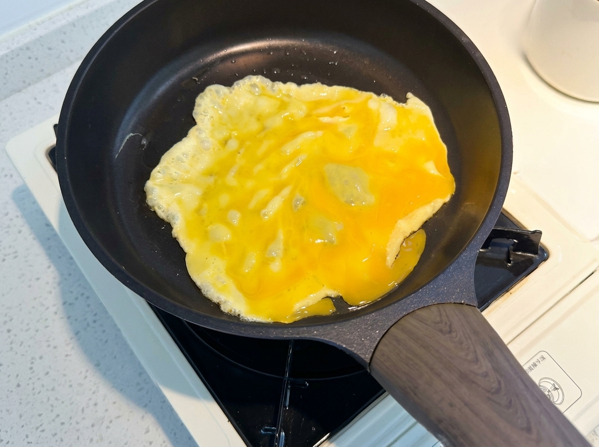 Yellow egg mixture cooking in a black non-stick frying pan.