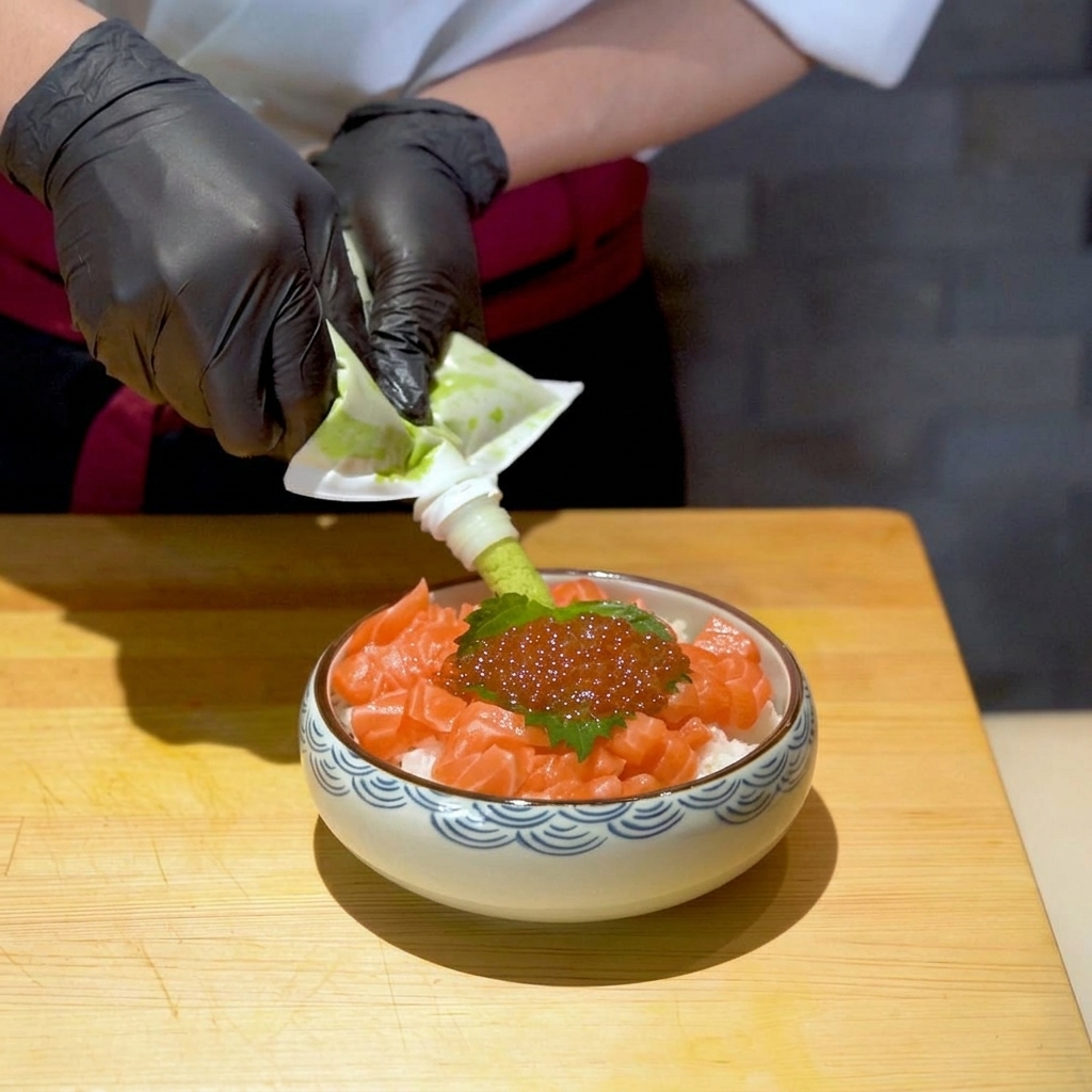 Squeezing vibrant green wasabi paste from a tube onto the finished raw salmon and ikura rice bowl.
