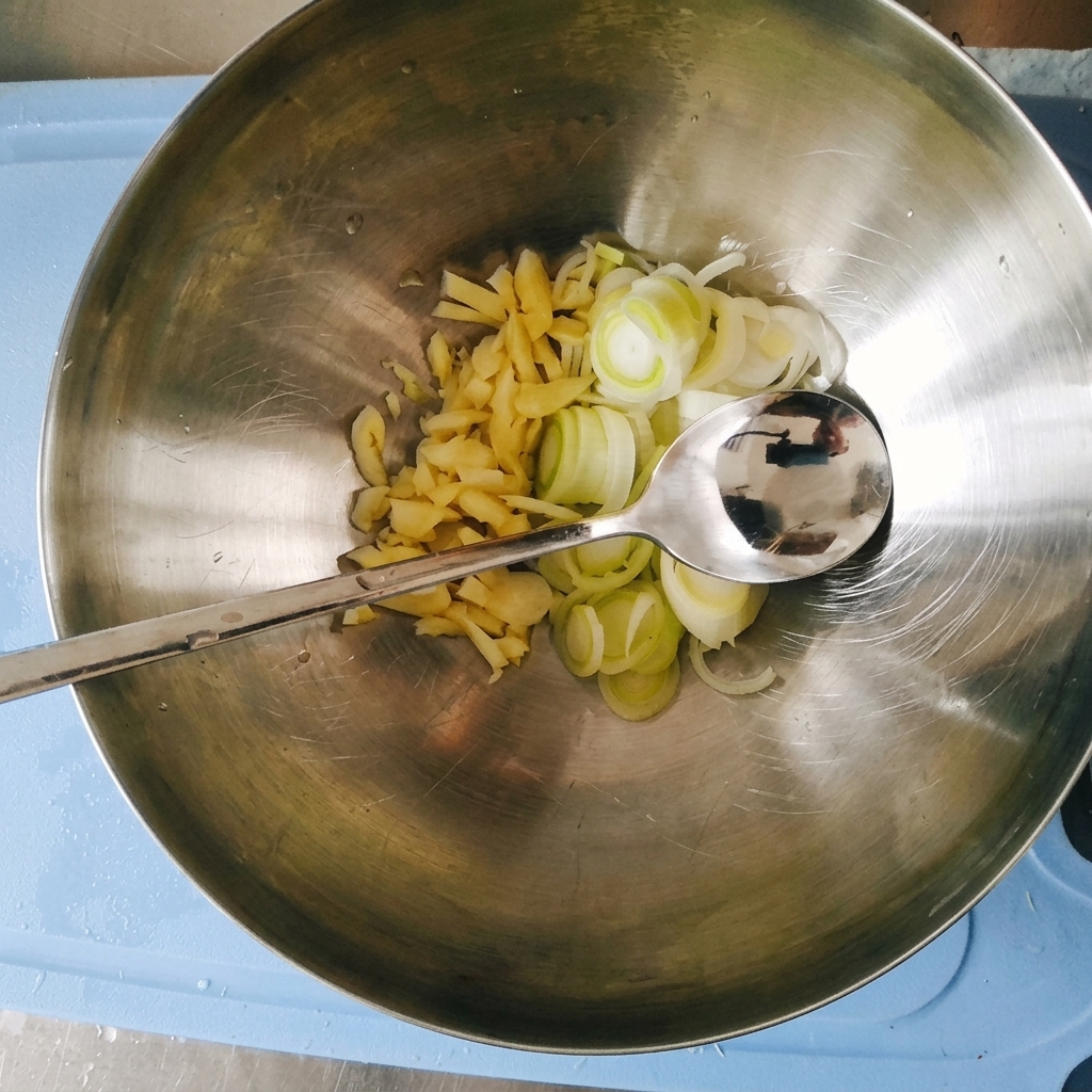 Finely chopped garlic and sliced green onions sitting together inside a large stainless steel mixing bowl with a metal spoon.