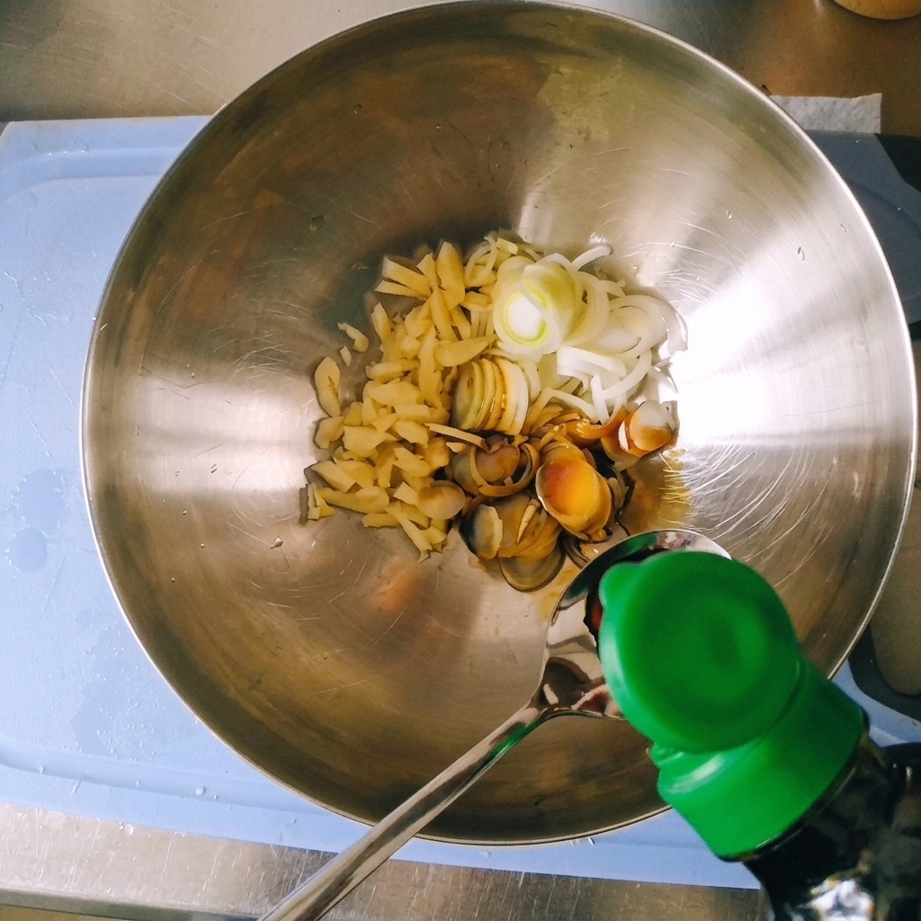 Pouring dark liquid soy sauce from a bottle into a spoon over a metal bowl containing sliced green onions and garlic.