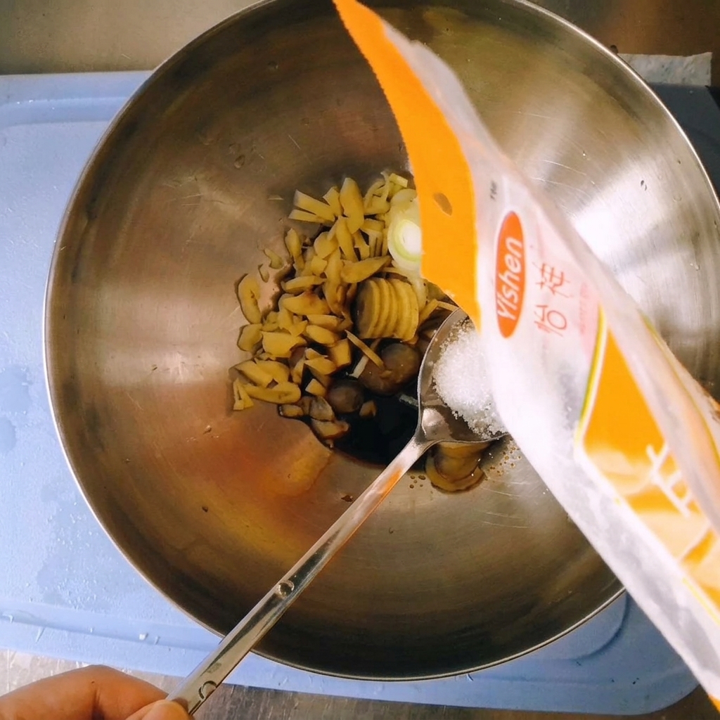 Pouring white granulated sugar from a plastic packaging bag onto a spoon held over the mixing bowl.