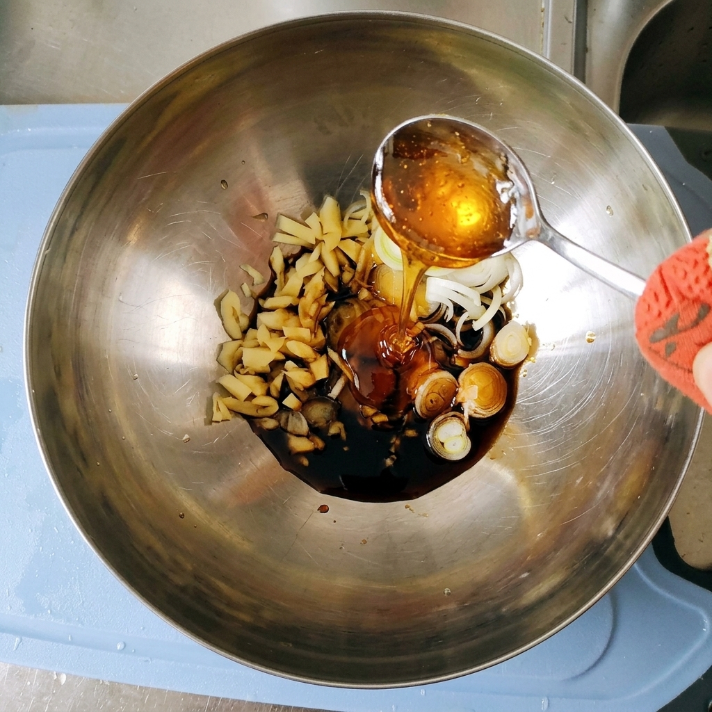 Thick, golden corn syrup being poured from a silver spoon into the marinade mixture inside the metal bowl.