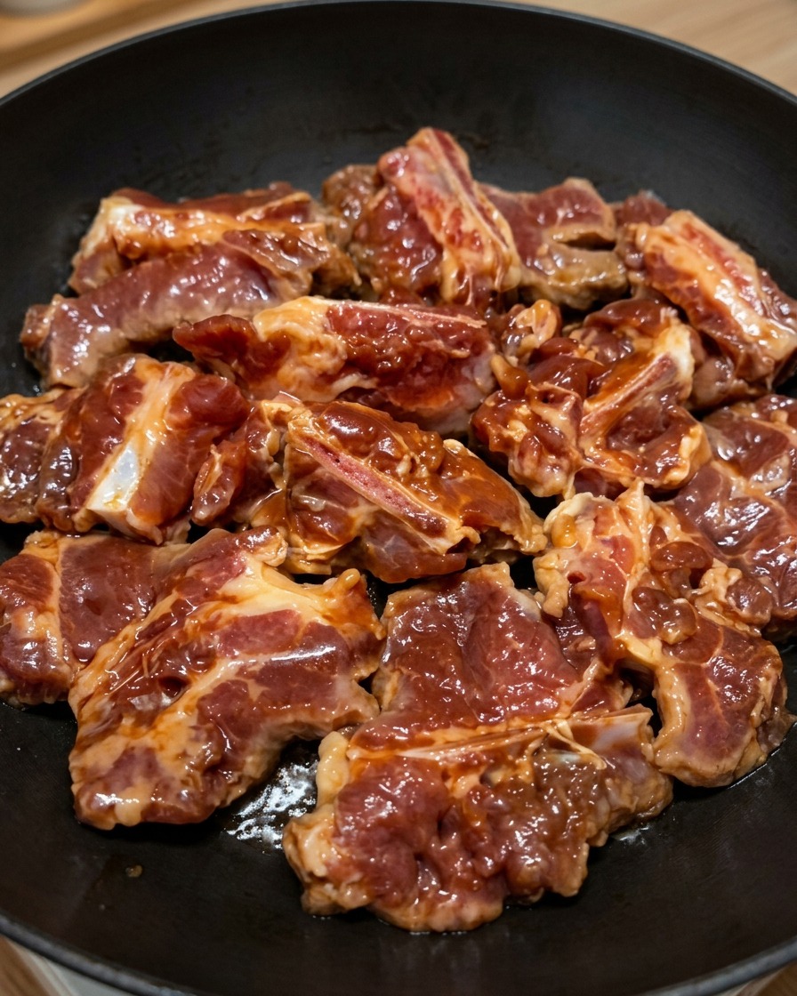 Marinated pork ribs neatly arranged in a single layer across a flat black frying pan.