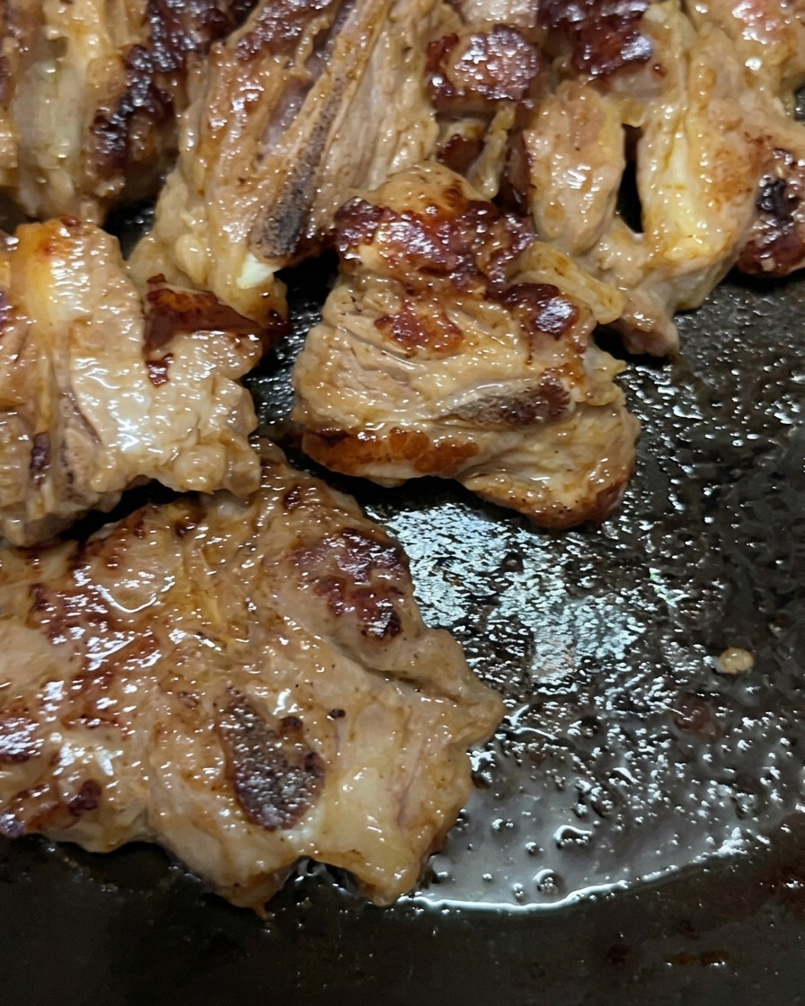 Pork ribs cooking in a pan, flipped over to reveal a deeply browned, caramelized surface.