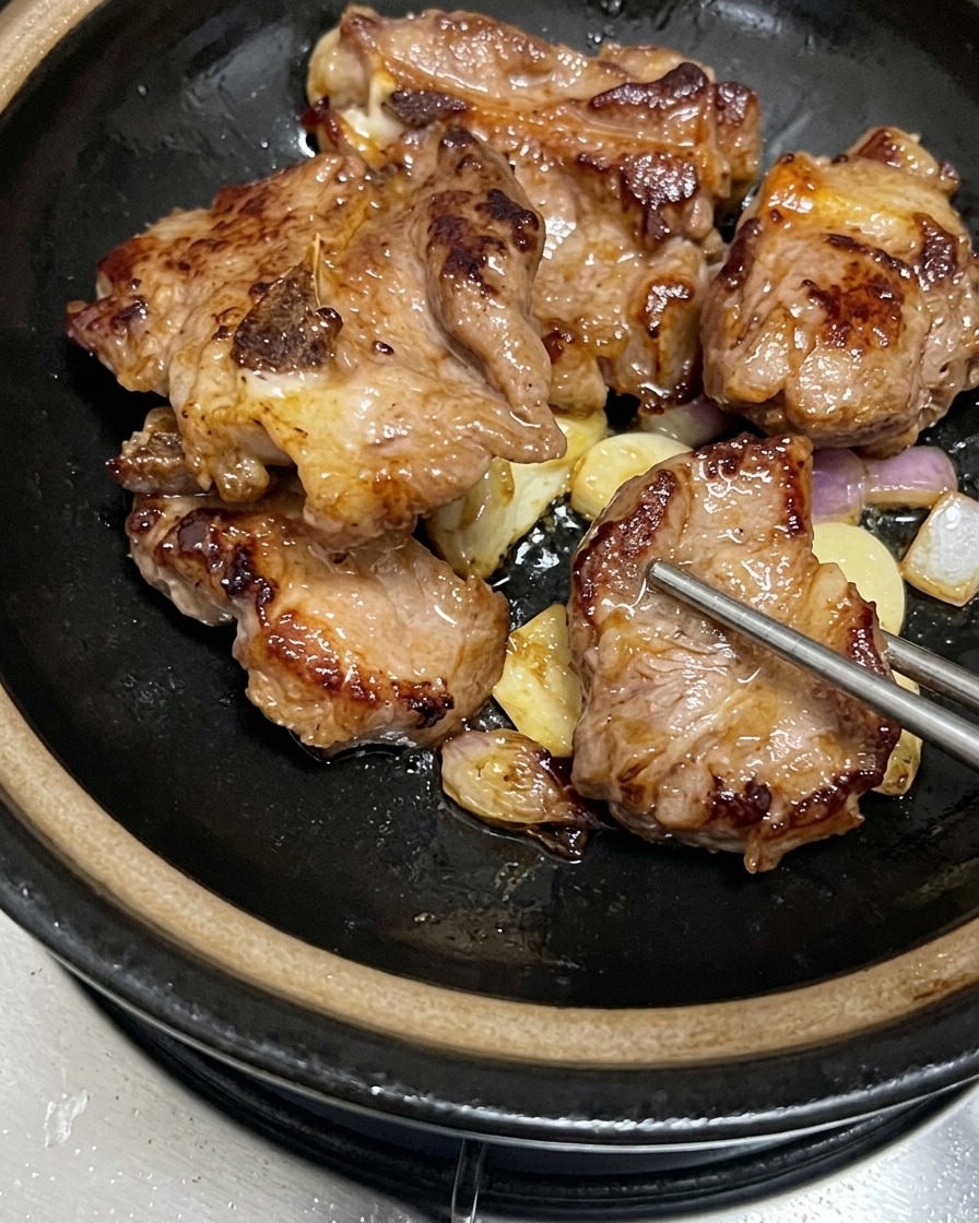 Seared golden-brown pork ribs arranged on top of browned garlic and shallots inside a black claypot.