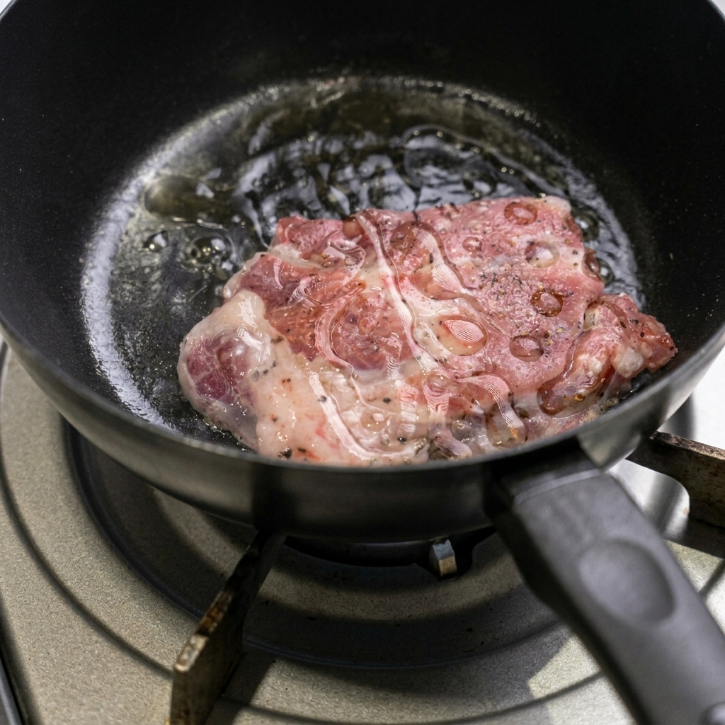 A seasoned raw pork chop searing inside a hot black pan with shimmering oil bubbling around the edges.