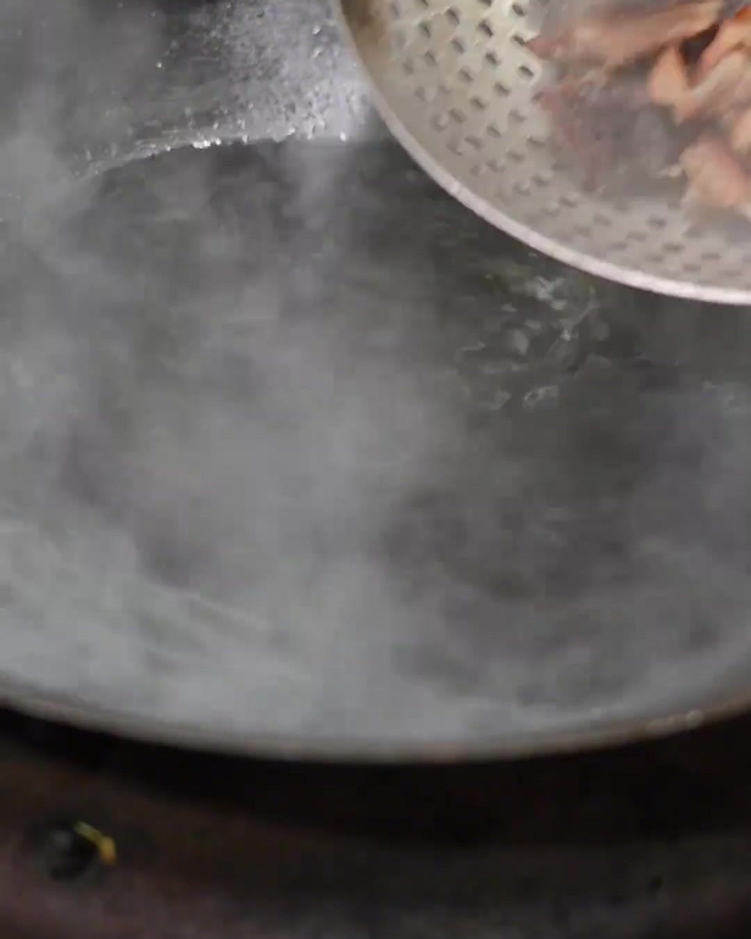 Cured ribs being strained and placed into a freshly boiling pot of clean water inside a wok.