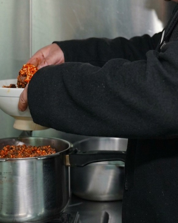 A white bowl filled with seasoned cured ribs being placed into a metal pressure cooker for steaming.
