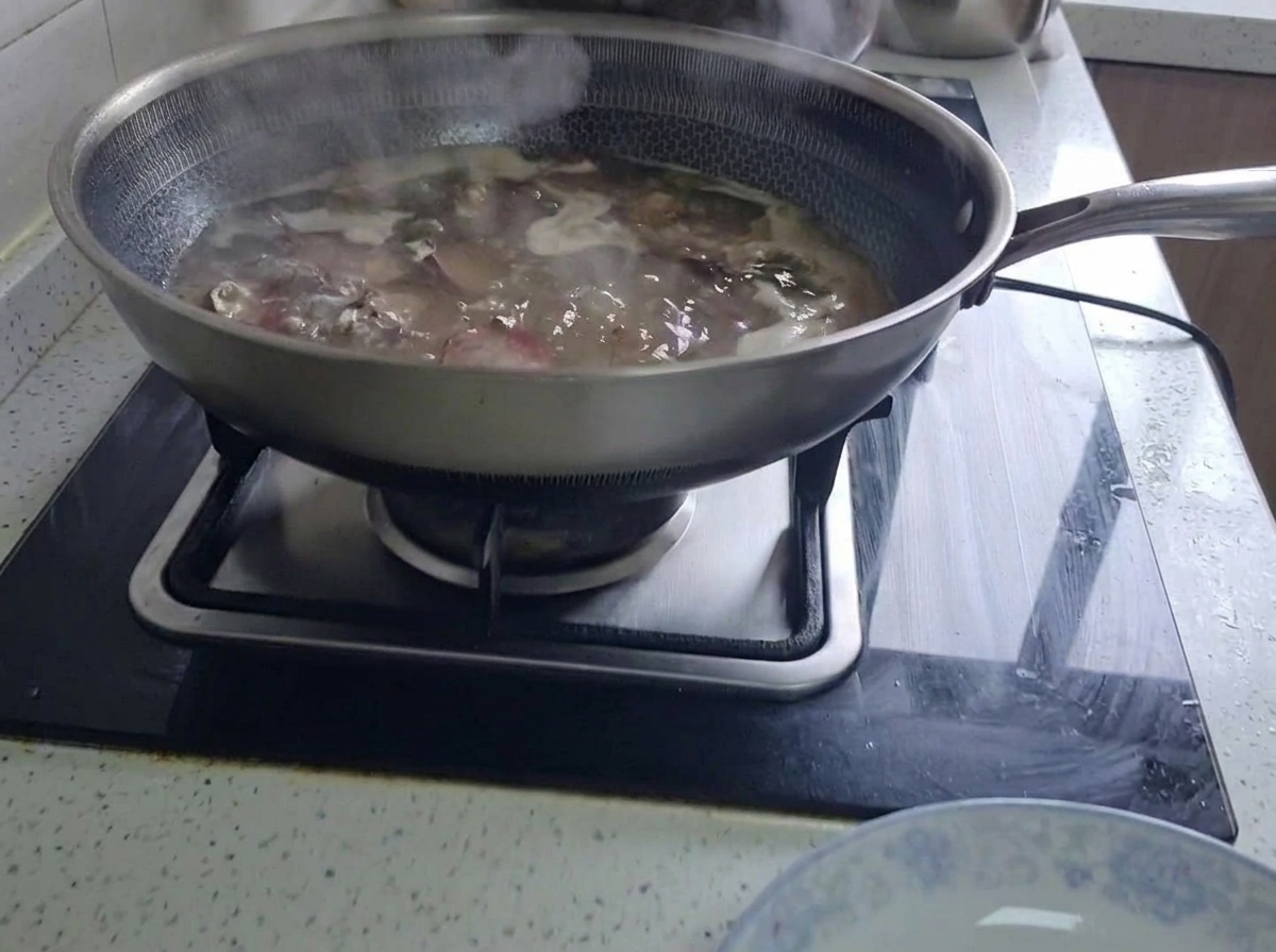 Cured pork ribs simmering in a large wok filled with boiling water on a kitchen stove.