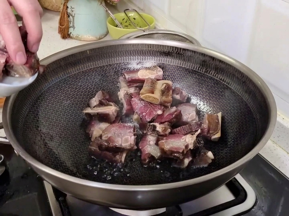 A hand transferring drained cured pork ribs from a small plate into a hot wok to stir-fry.