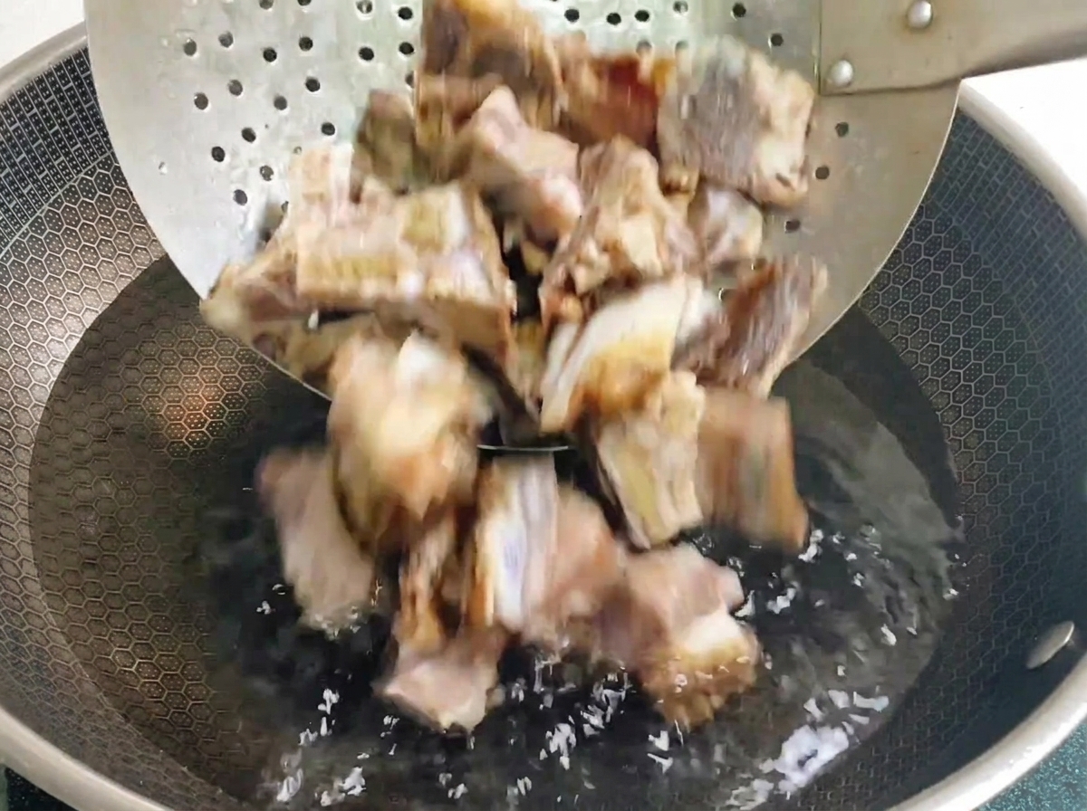Cured pork ribs being transferred from a metal skimmer into a wok filled with cold water.