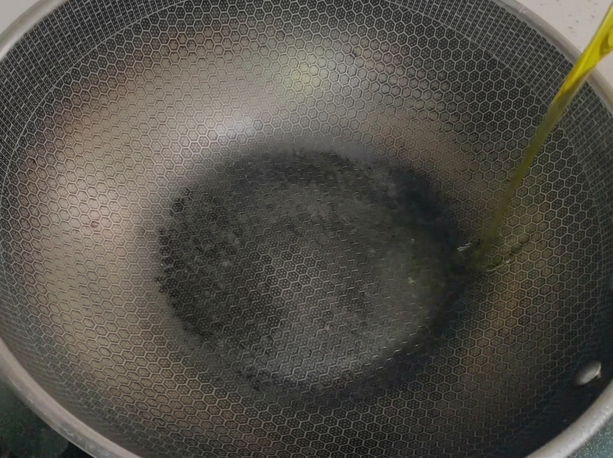 A steady stream of golden camellia oil being poured into a heated, honeycomb-patterned wok.