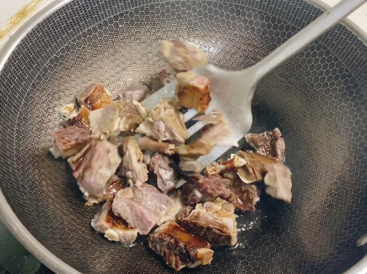 Blanched pieces of pork ribs being tossed with a metal spatula in a honeycomb wok to render out the fat.