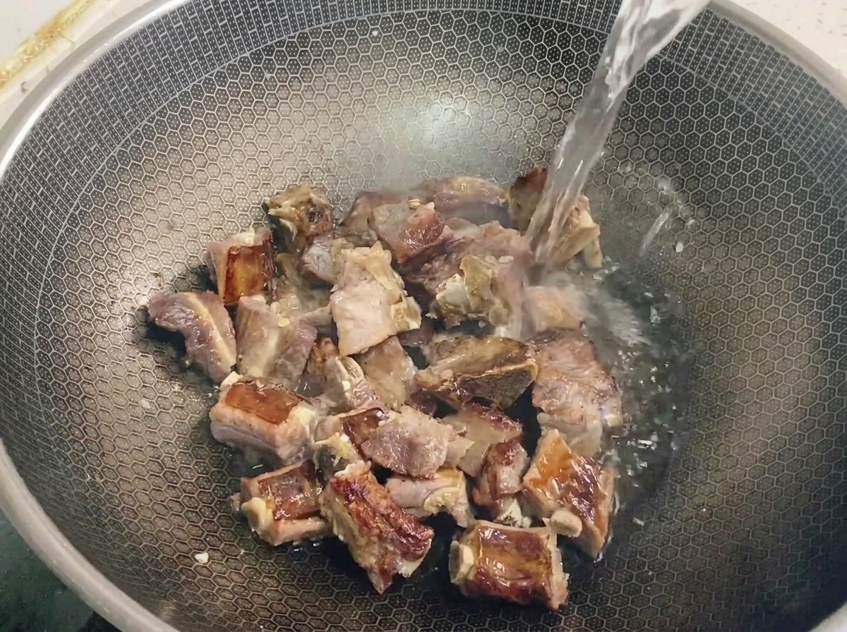 A clear liquid being poured over stir-frying pork ribs in a honeycomb wok.