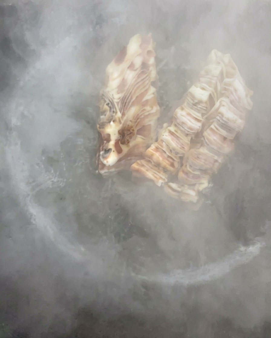 Cured pork ribs boiling in a large pot of water filled with rising steam.