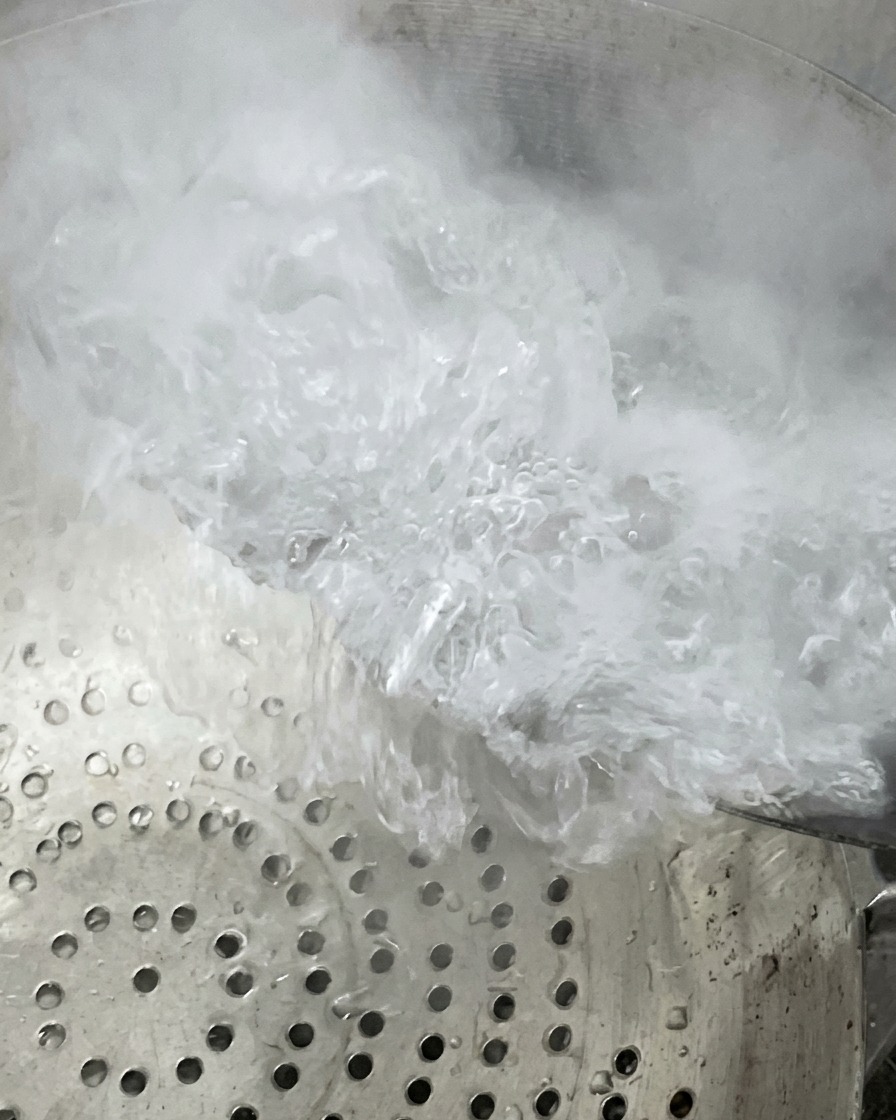 Boiling water and steam rising as the content is being poured or transferred over a metal strainer colander.