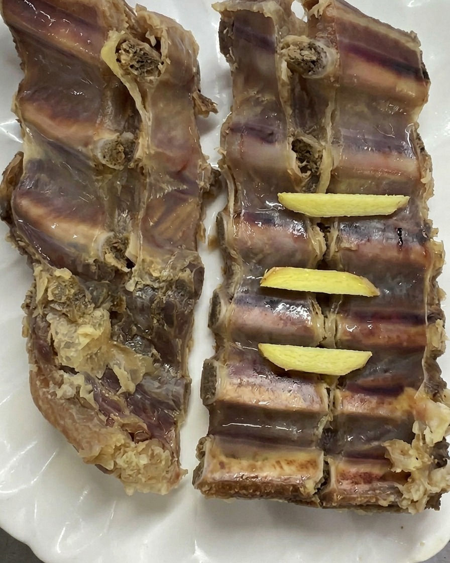 Two slabs of blanched pork ribs arranged on a white plate with fresh yellow ginger pieces placed neatly on top.