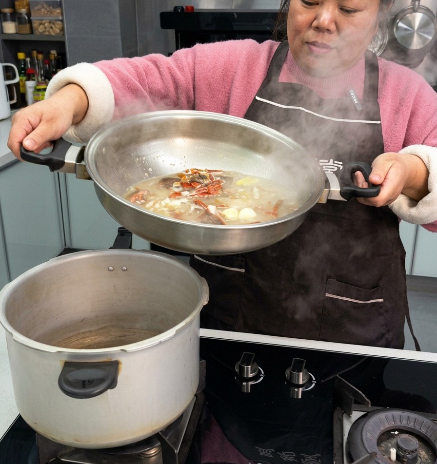 A person pouring a rich broth with cured pork ribs, garlic, and dried chilies from a stainless steel pan into a pressure cooker pot.