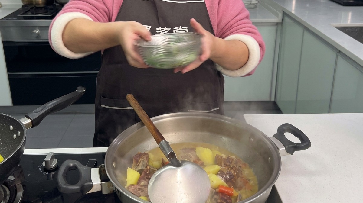 Chopped green garlic sprouts being added from a clear bowl into a steaming wok filled with stewed cured pork ribs and roll-cut potatoes.