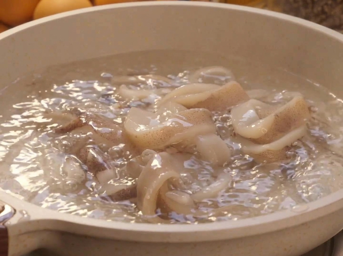 Fresh white squid rings blanching inside a pot of rapidly boiling water.